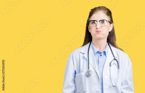 Middle age mature doctor woman wearing medical coat over isolated background puffing cheeks with funny face. Mouth inflated with air  crazy expression.