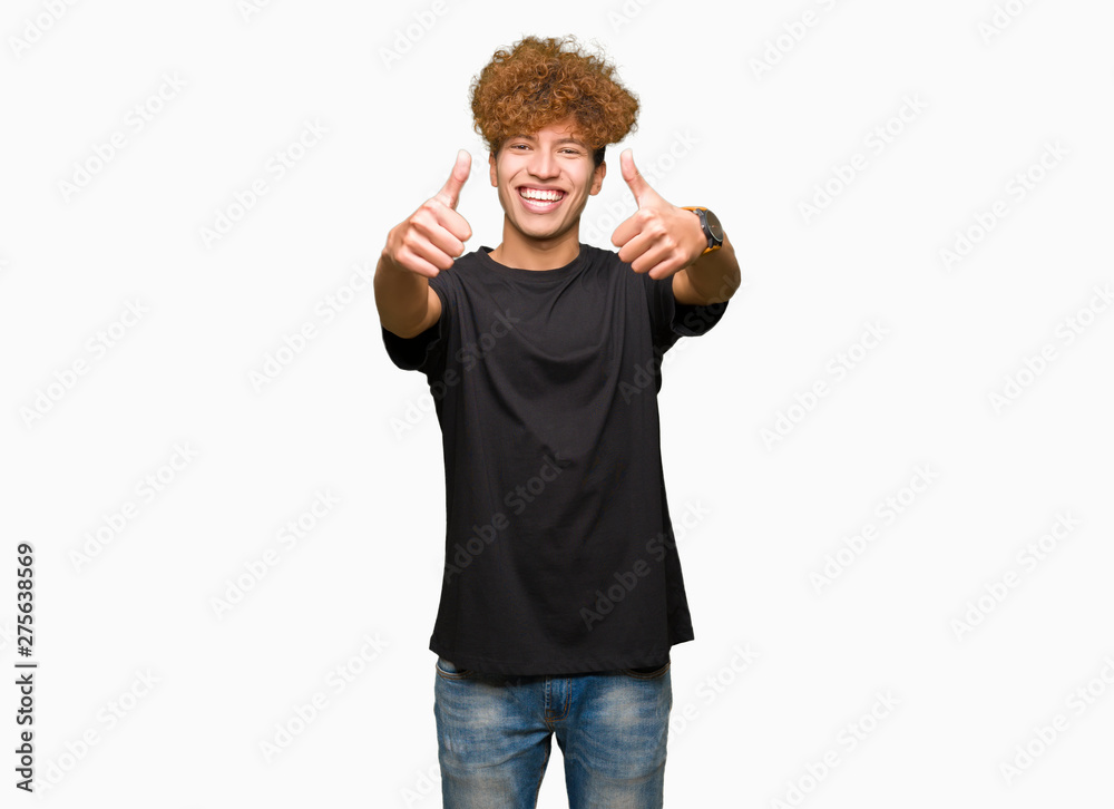 Fototapeta premium Young handsome man with afro hair wearing black t-shirt approving doing positive gesture with hand, thumbs up smiling and happy for success. Looking at the camera, winner gesture.