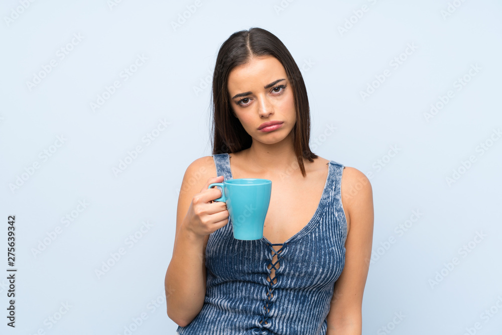 Young woman over isolated blue wall holding hot cup of coffee Young woman over isolated blue wall holding hot cup of coffee