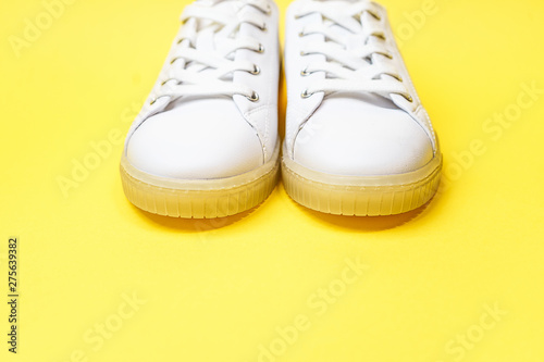 White sneakers are lying on a bright yellow background. Top view. Flat lay. Copy space. Black Friday, party, sport concept, outfit.