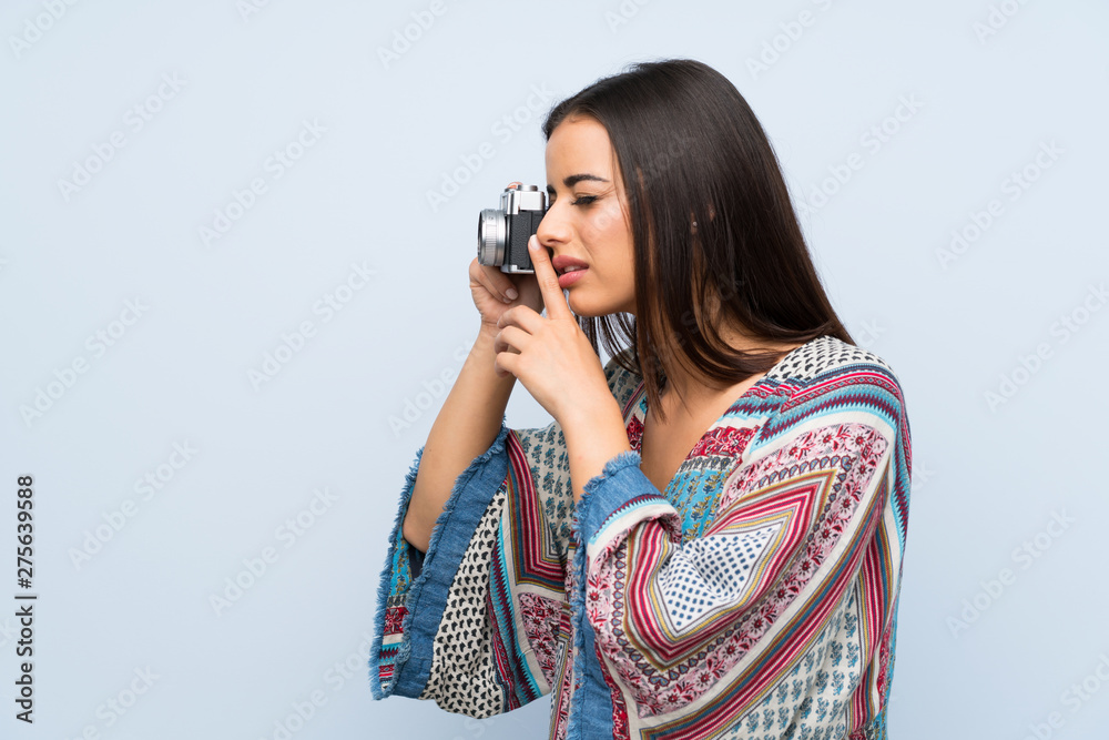 Young woman over isolated blue wall holding a camera Young woman over isolated blue wall holding a camera