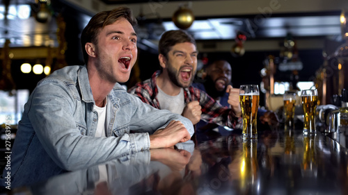 Emotional male fans cheering for favorite team in pub, celebrating game victory