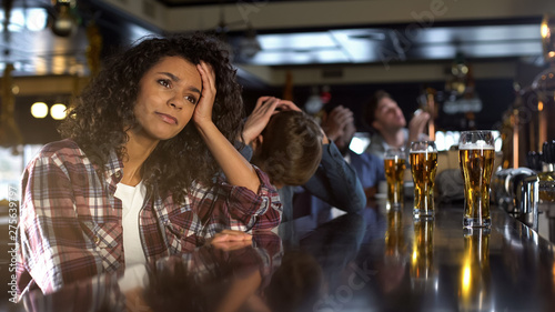 Tableau sur toile Disappointed biracial female with male friends watching sport game in bar, loss
