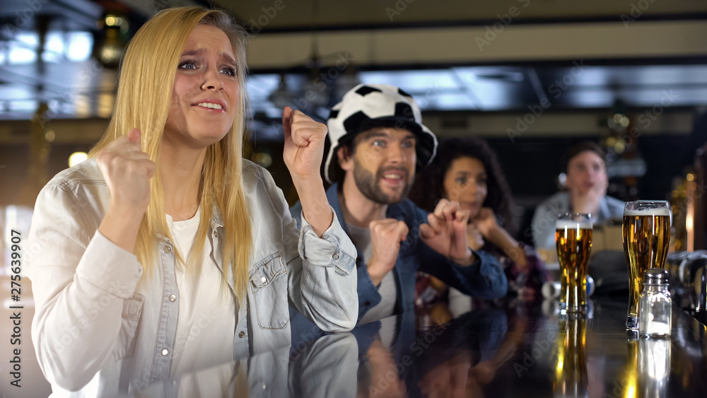 Fototapeta premium Anxious blond lady sports fan crossing fingers, spectators watching game in pub