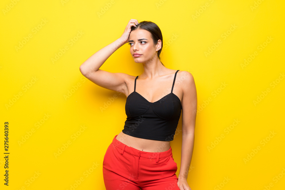 Young woman over isolated yellow background having doubts while scratching head Young woman over isolated yellow background having doubts while scratching head