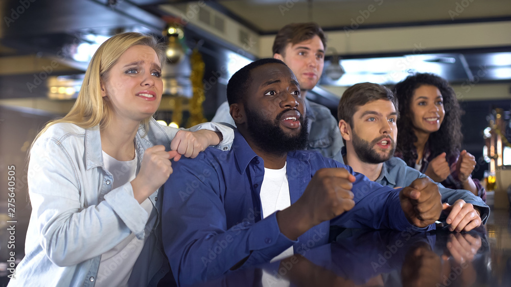 Multiethnic company watching sport game together in bar, upset about losing game Multiethnic company watching sport game together in bar, upset about losing game