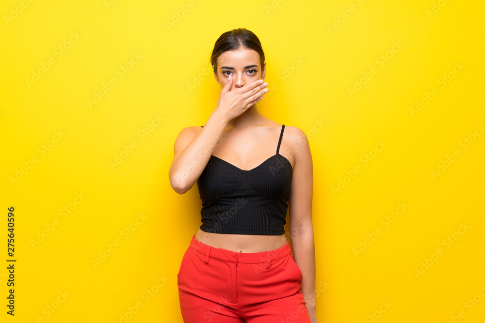 Young woman over isolated yellow background covering mouth with hands Young woman over isolated yellow background covering mouth with hands
