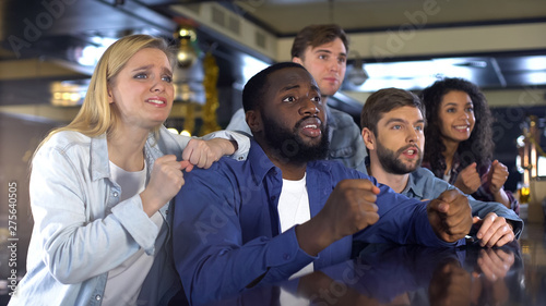 Multiethnic company watching sport game together in bar, upset about losing game