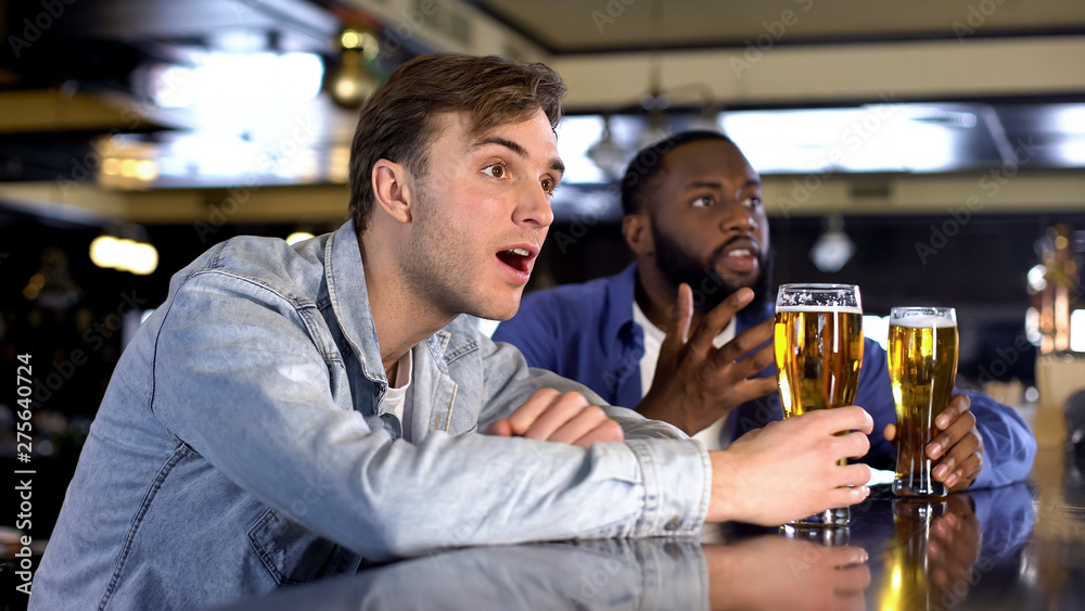Nervous male friends attentively watching sport match drinking beer, support