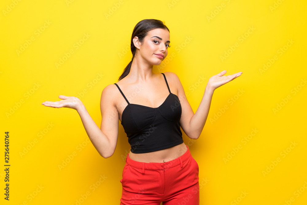 Young woman over isolated yellow background making doubts gesture