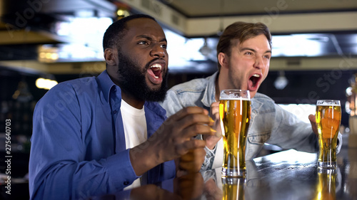Two young men watching sport competition in pub, holding beer glasses, hobby