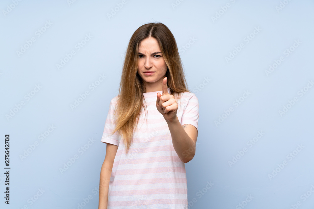 Young woman over isolated blue background frustrated and pointing to the front