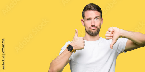Handsome man wearing casual white t-shirt Doing thumbs up and down, disagreement and agreement expression. Crazy conflict photo