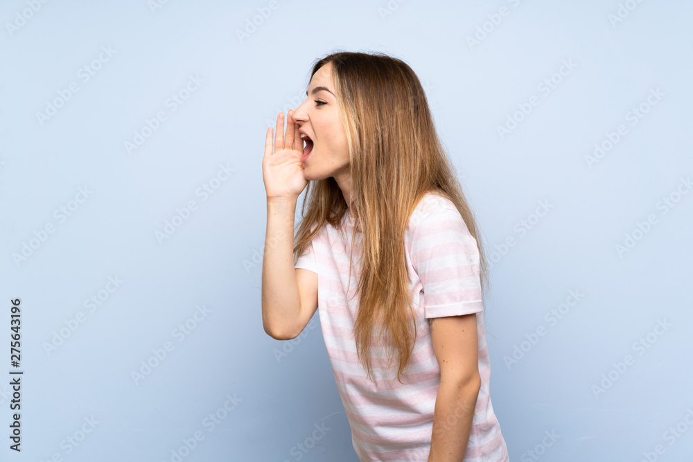 Young woman over isolated blue background shouting with mouth wide open to the lateral Young woman over isolated blue background shouting with mouth wide open to the lateral