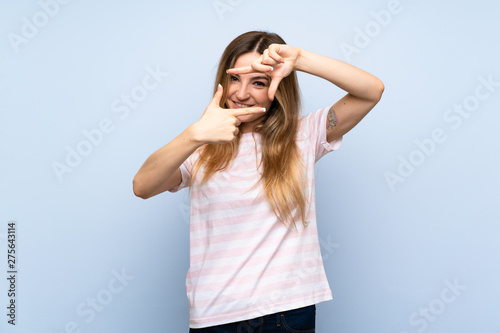 Young woman over isolated blue background focusing face. Framing symbol