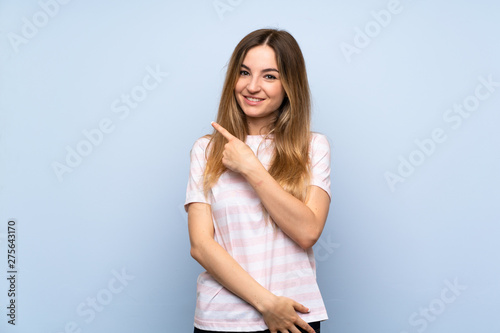 Young woman over isolated blue background pointing to the side to present a product
