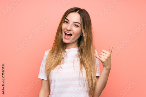 Young woman over isolated pink wall making phone gesture