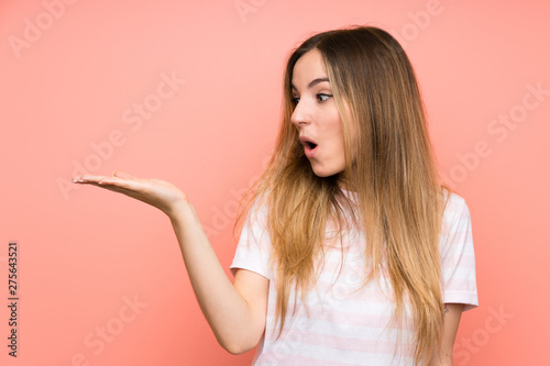 Young woman over isolated pink wall holding copyspace imaginary on the palm