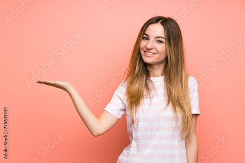 Young woman over isolated pink wall holding copyspace imaginary on the palm