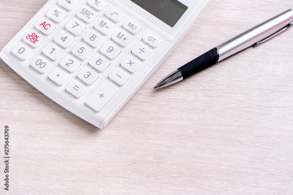 White calculator and pen on bright wooden table, analytics and statistics of financial profit, investment risk concept, copy space, top view flat lay White calculator and pen on bright wooden table, analytics and statistics of financial profit, investment risk concept, copy space, top view flat lay