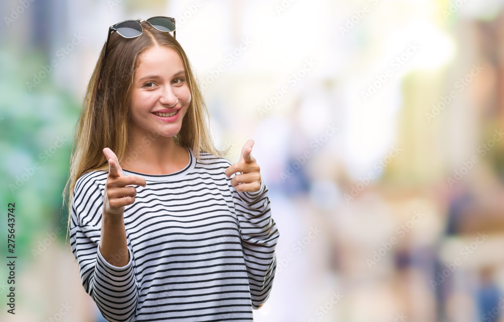 Young beautiful blonde woman wearing sunglasses over isolated background pointing fingers to camera with happy and funny face. Good energy and vibes.