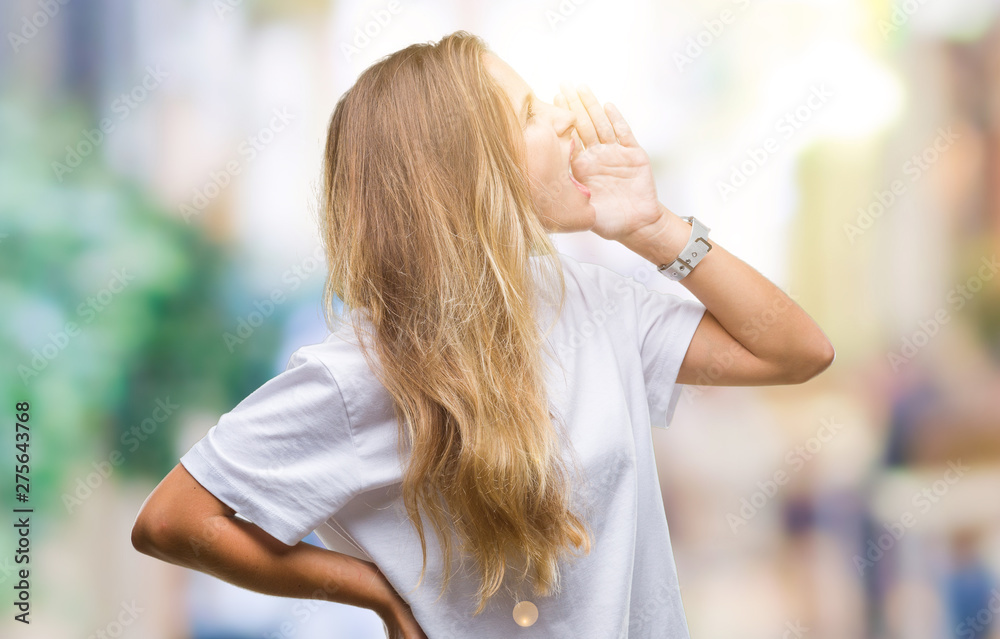 Young beautiful blonde woman wearing casual white t-shirt over isolated background shouting and screaming loud to side with hand on mouth. Communication concept.