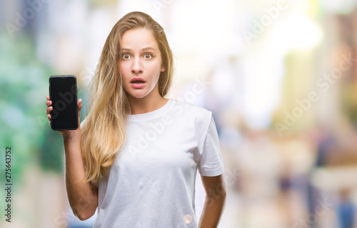 Young beautiful blonde woman showing screen of smartphone over isolated background scared in shock with a surprise face, afraid and excited with fear expression © Krakenimages.com