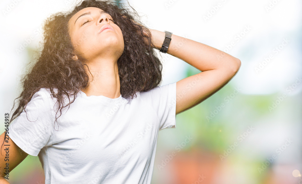 Young beautiful girl with curly hair wearing casual white t-shirt stretching back, tired and relaxed, sleepy and yawning for early morning