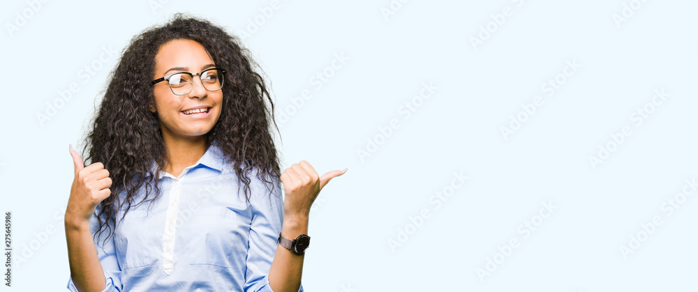 Young beautiful business girl with curly hair wearing glasses success sign doing positive gesture with hand, thumbs up smiling and happy. Looking at the camera with cheerful expression