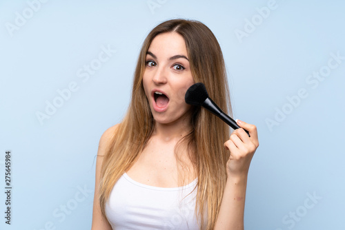 Young woman over isolated blue background with makeup brush