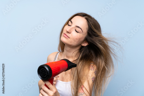 Young woman over isolated blue background with hairdryer