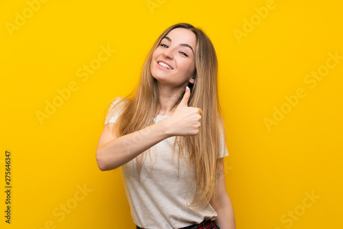 Young woman over isolated yellow wall giving a thumbs up gesture