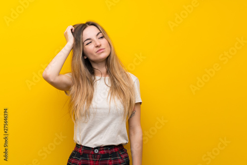 Young woman over isolated yellow wall having doubts and with confuse face expression