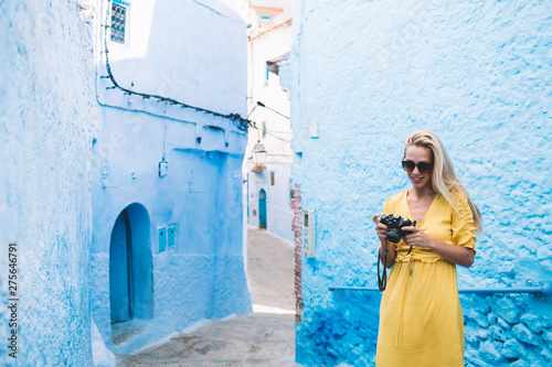 Skilled female journalist standing at street of ancient city - Morocco editing pictures of architecture Unesco buildings, attractive woman in stylish sunglasses checking photos on retro equipment © BullRun