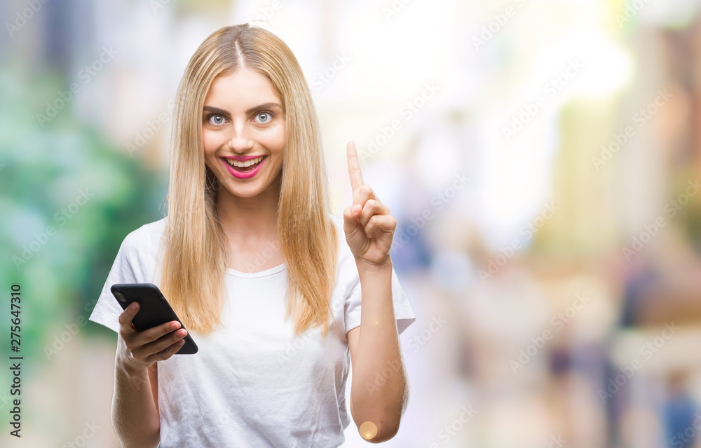 Fototapeta premium Young beautiful blonde woman using smartphone over isolated background surprised with an idea or question pointing finger with happy face, number one