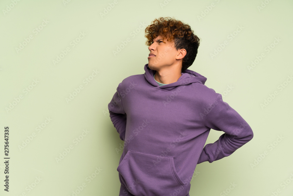 Young african american man over isolated green wall suffering from backache for having made an effort Young african american man over isolated green wall suffering from backache for having made an effort