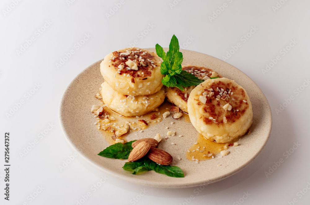 Delicious breakfast - cottage cheese pancakes, cheesecakes, cottage cheese pancakes with almonds, mint and maple syrup in a beige plate. Useful dessert on white background (isolate)