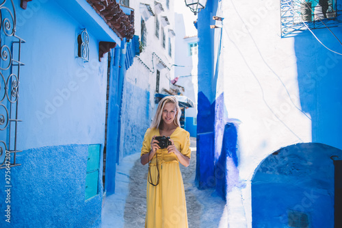 Portrait of woman with retro camera enjoying free day in Chaouen historic center, positive female photographer exploring Morocco during vacations using vintage equipment for recreating with hobby © BullRun