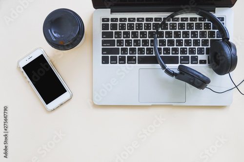 Coffee cup; cellphone and headphone over the laptop against beige background