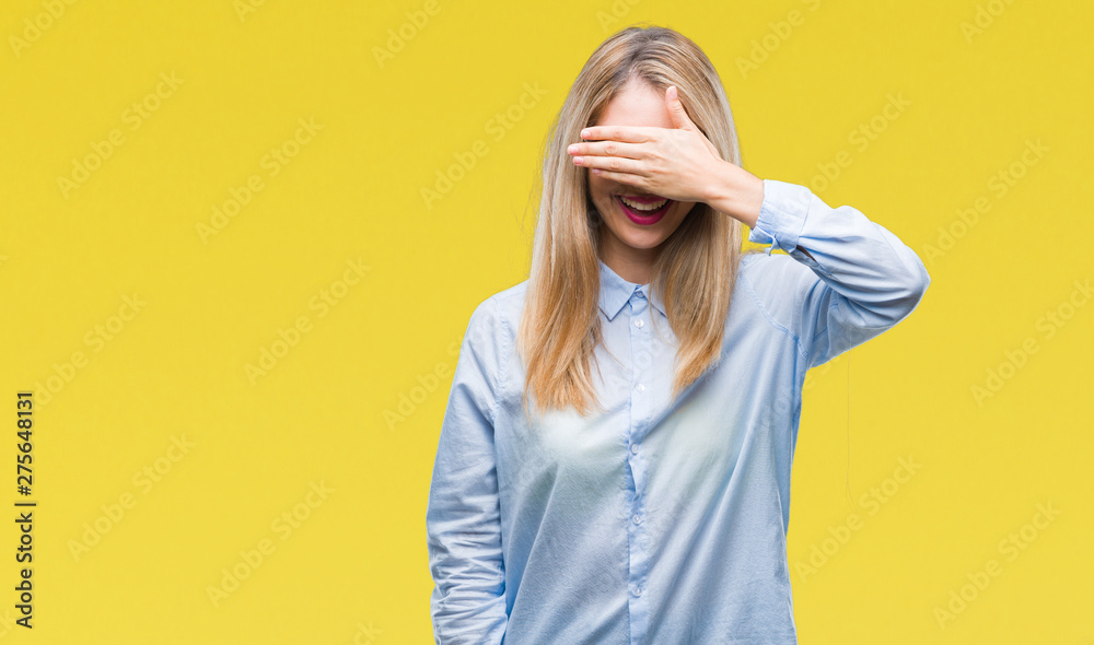 Young beautiful blonde business woman wearing glasses over isolated background smiling and laughing with hand on face covering eyes for surprise. Blind concept. Young beautiful blonde business woman wearing glasses over isolated background smiling and laughing with hand on face covering eyes for surprise. Blind concept.
