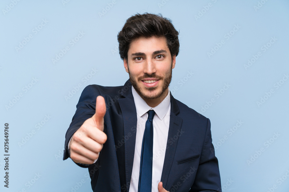 Businessman over isolated blue wall with thumbs up because something good has happened Businessman over isolated blue wall with thumbs up because something good has happened