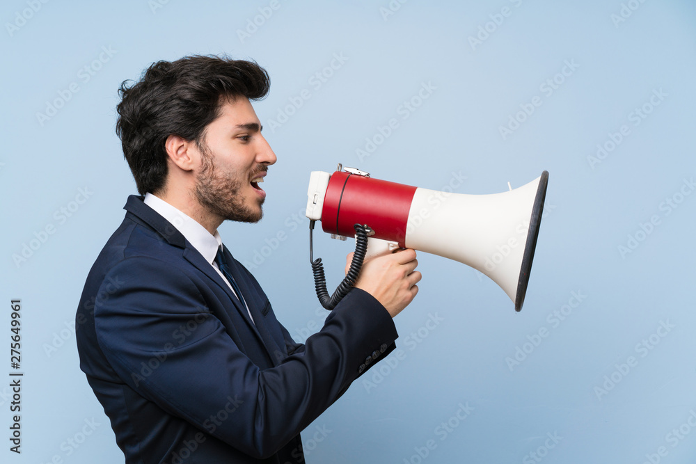Businessman over isolated blue wall shouting through a megaphone Businessman over isolated blue wall shouting through a megaphone