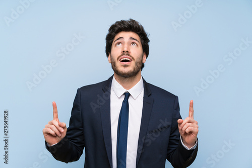 Businessman over isolated blue wall surprised and pointing up