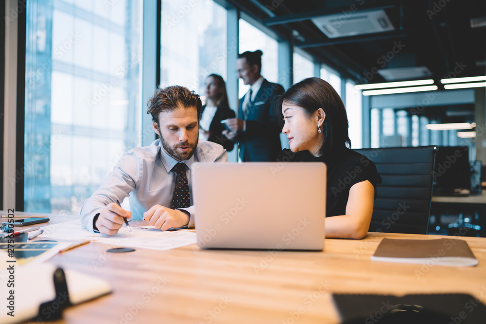 Serious male and female financial experts checking information during accounting process near desktop with modern laptop computer, mature diverse colleagues consultancy about report of startup project