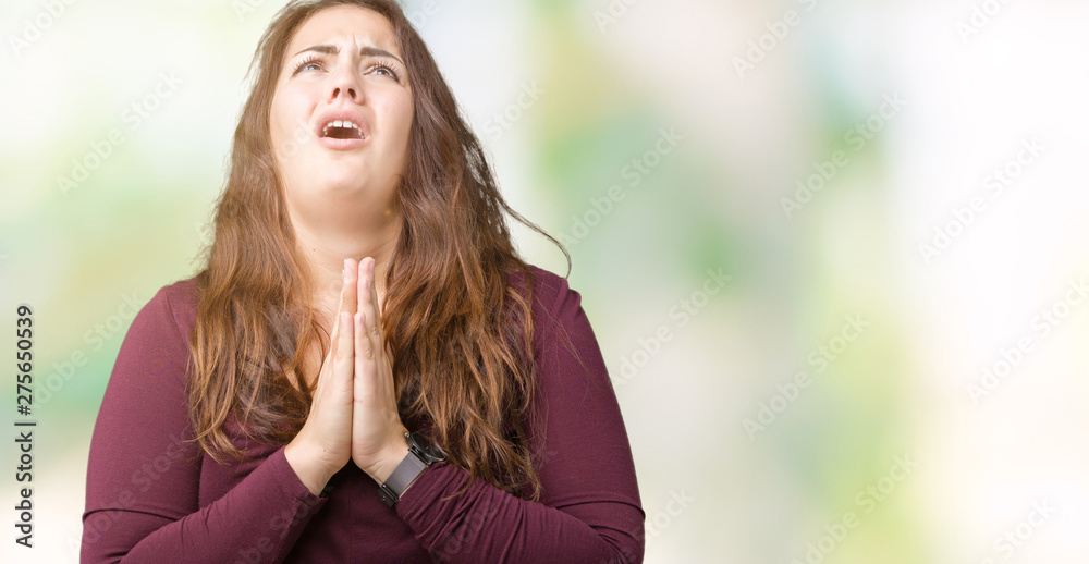 Beautiful and attractive plus size young woman wearing a dress over isolated background begging and praying with hands together with hope expression on face very emotional and worried. 