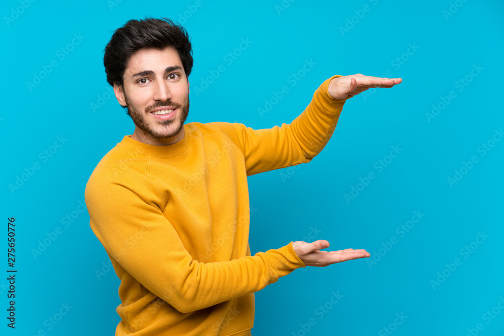Handsome over isolated blue wall holding copyspace to insert an ad