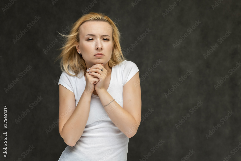 Waist up portrait of pretty interesting fashionable blonde girl on gray background in white t-shirt. Standing in front of the camera, smiling, showing hands. Shows a lot of emotions. Waist up portrait of pretty interesting fashionable blonde girl on gray background in white t-shirt. Standing in front of the camera, smiling, showing hands. Shows a lot of emotions.