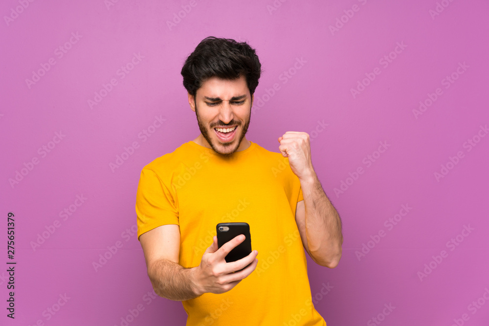 Handsome over isolated purple wall with phone in victory position Handsome over isolated purple wall with phone in victory position
