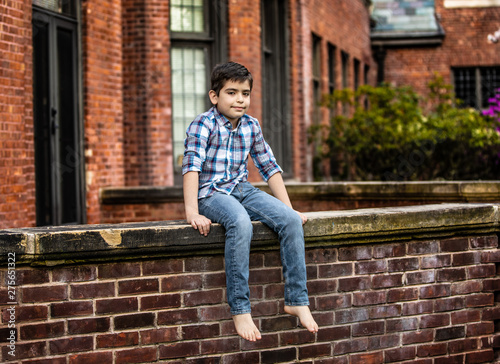Boy sitting on brick wall in jeans and plaid shirt