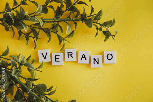 The inscription verano in spanish on the letters of the keyboard on a yellow background with branches of flowers photo